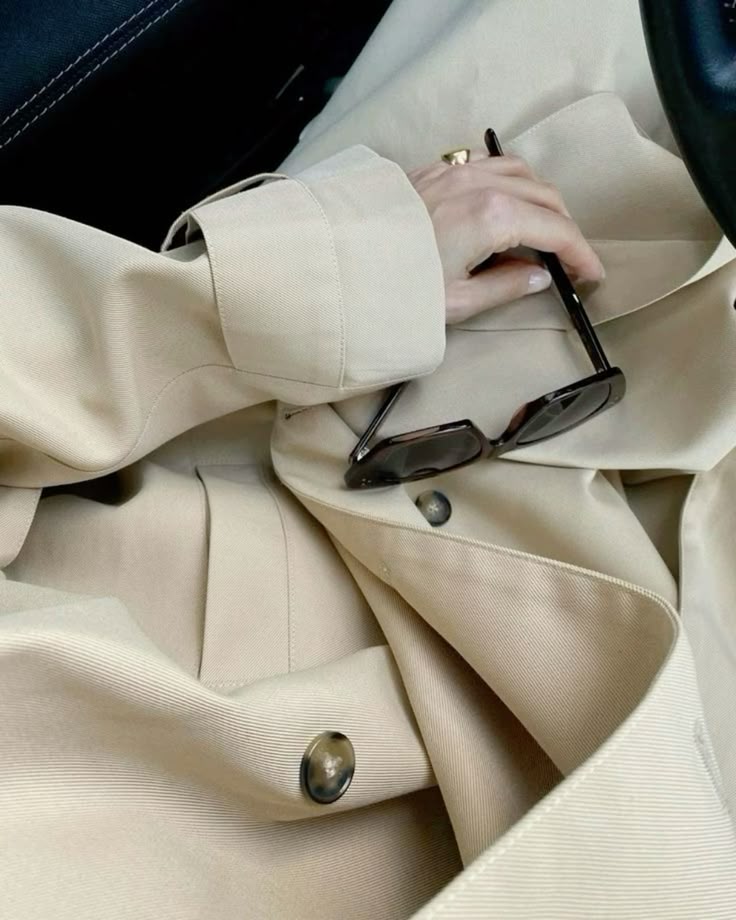 A hand resting on a camel trench cuff, sunglasses tucked in